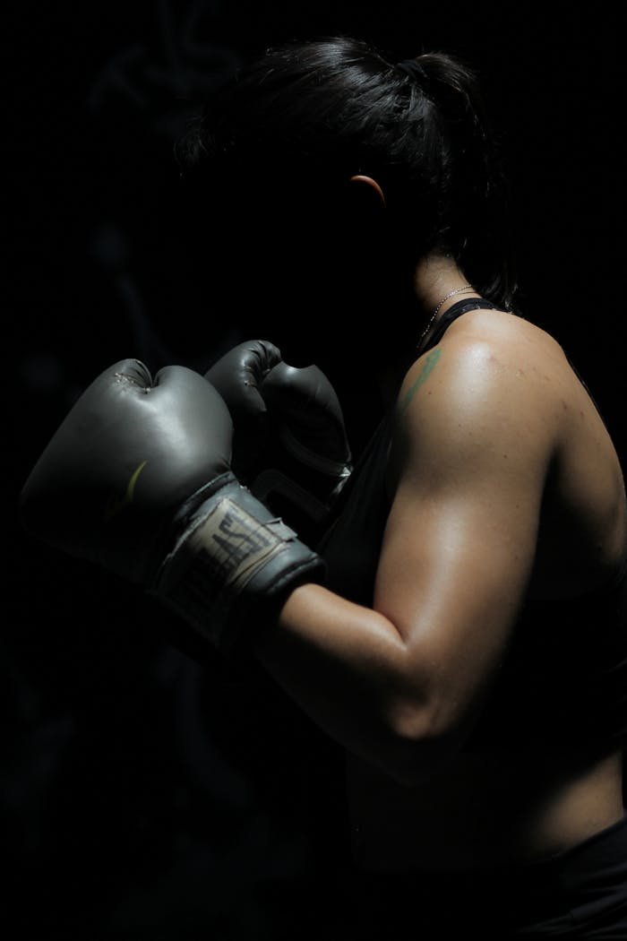 A powerful image of a female boxer showcasing strength and determination in a dark setting.